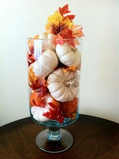 a glass vase filled with white and orange pumpkins on top of a wooden table