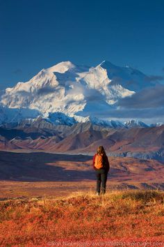 a woman standing on top of a grass covered field next to a snow covered mountain