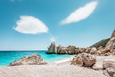 the beach is clear and blue with some rocks on it's shore, under a cloud in the sky