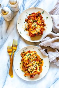 two white plates topped with lasagna covered in cheese and sauce next to silverware