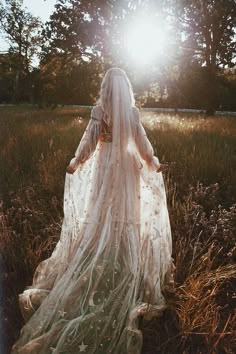 a woman in a white wedding dress walking through tall grass with the sun shining behind her