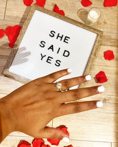 a woman's hand with white nails and red rose petals on the floor next to a sign that says she said yes