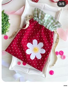 a red and white polka dot dress with a flower on the front, sitting next to a green potted plant