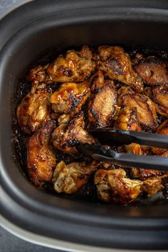 a slow cooker filled with chicken wings and sauce being spooned into the pot