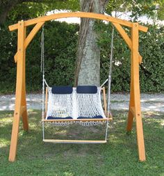 a hammock hanging from a wooden frame in the grass next to a tree