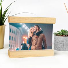 a wooden frame with an image of a man and woman holding each other in front of a potted plant