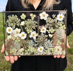 a woman is holding a glass box with flowers on it