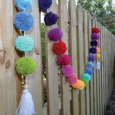 colorful pom - poms hanging on the side of a wooden fence