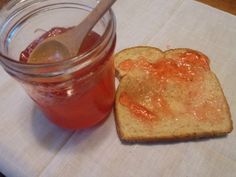 a sandwich with jelly on it next to a jar of jelly and a spoon sitting on a table