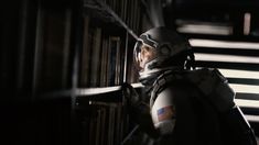 a man in an astronaut suit standing next to a bookshelf