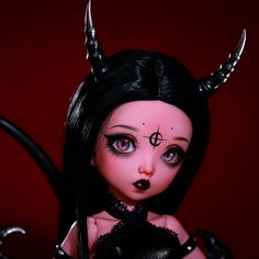 a doll with black hair and horns on her head is posed in front of a red background