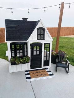 a small white house sitting on top of a cement floor next to a black chair