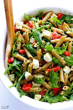 a white bowl filled with pasta and spinach salad next to wooden utensils