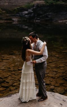 a bride and groom kissing on the rocks by the water