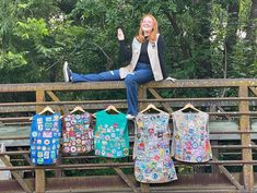 a woman sitting on top of a wooden bench next to lots of t - shirts