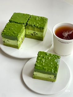 three pieces of green cake on plates next to a cup of tea