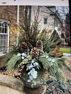 a potted plant with pine cones and greenery in front of a brick building