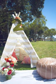 a teepee sitting on top of a lush green field next to a vase filled with flowers