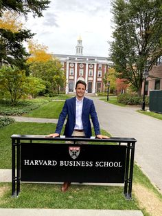 a man standing behind a black sign in front of a building with trees and grass