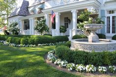 a large white house with a fountain in the front yard and flowers on the lawn