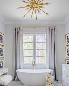 a white bathtub sitting under a chandelier in a bathroom next to a window