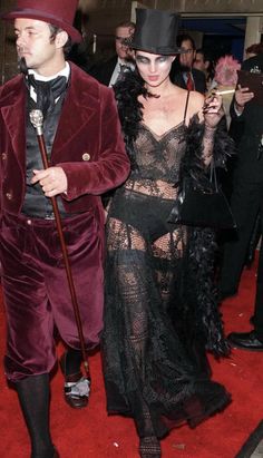 a man and woman dressed in costume walking down a red carpeted area with other people