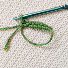 the crochet hook has been hooked up with a green thread and is on top of a white knitted surface