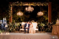 a bride and groom sitting on a couch under a chandelier at their wedding