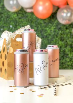 three pink and white can coolers sitting on top of a table with balloons in the background