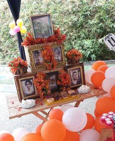 a table topped with pictures and balloons in front of a tree filled with orange flowers