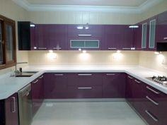 an empty kitchen with purple cabinets and white counter tops, lights on above the sink