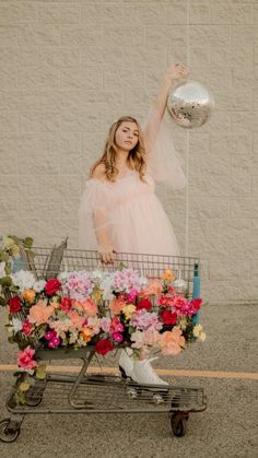 a woman standing in front of a shopping cart filled with flowers and holding a silver ball