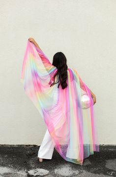 a woman in white pants is holding a pink and blue shawl over her head