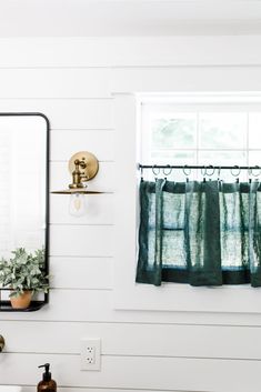 a bathroom with a sink, mirror and green curtains in the window sill on the wall