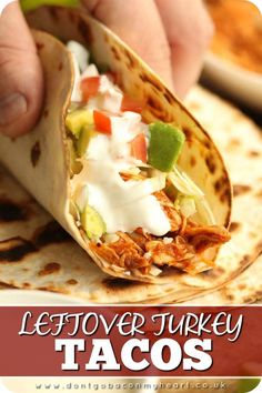 a hand holding a tortilla filled with chicken, avocado and sour cream