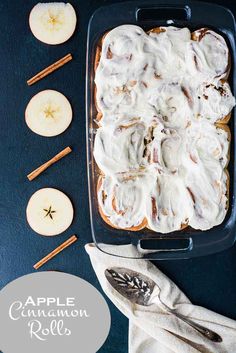 an apple cinnamon roll with icing in a glass baking dish next to apples and cinnamon sticks