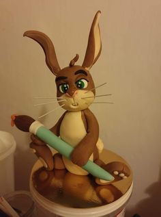 a cake that looks like a rabbit holding a pencil in it's paws and sitting on top of a trash can