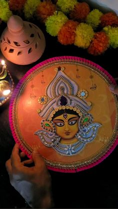 a person holding a plate with a painting on it next to some candles and flowers