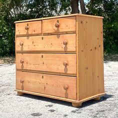 a wooden dresser sitting on top of a cement ground next to a tree and bushes