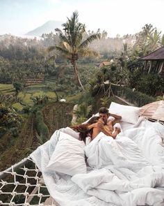 a man and woman laying in bed on top of a hammock next to rice fields