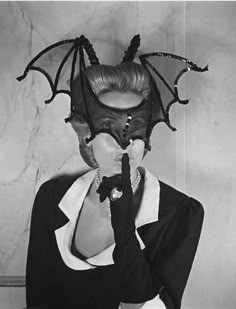 a woman wearing a bat mask with her hands to her mouth and the other hand in front of her face