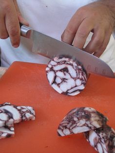 a man cutting up food on top of an orange cutting board with a large knife