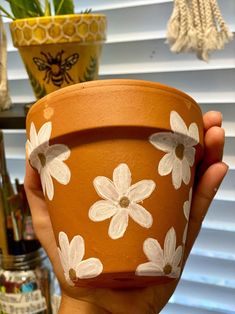 a hand holding a clay pot with flowers painted on it