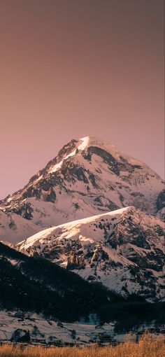 a large mountain covered in snow under a pink sky