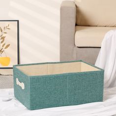 a blue storage box sitting on top of a bed next to a white chair and painting