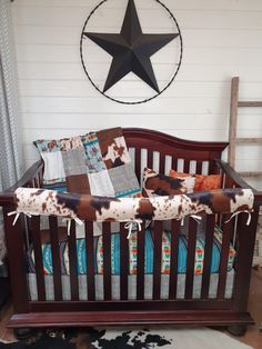 a baby crib with a cow print blanket on it and a black star hanging above the crib