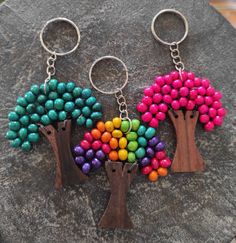 two key chains with colorful beads on them are sitting on a rock, one is shaped like a tree and the other is made out of wood