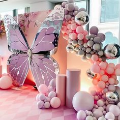 a pink and white table topped with balloons and a large butterfly decoration on top of it