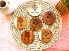 four personalized wooden coasters sitting on a wicker plate next to a potted plant