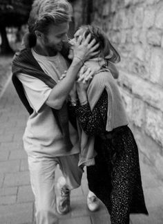 a man and woman walking down the street together, one is kissing the other's forehead